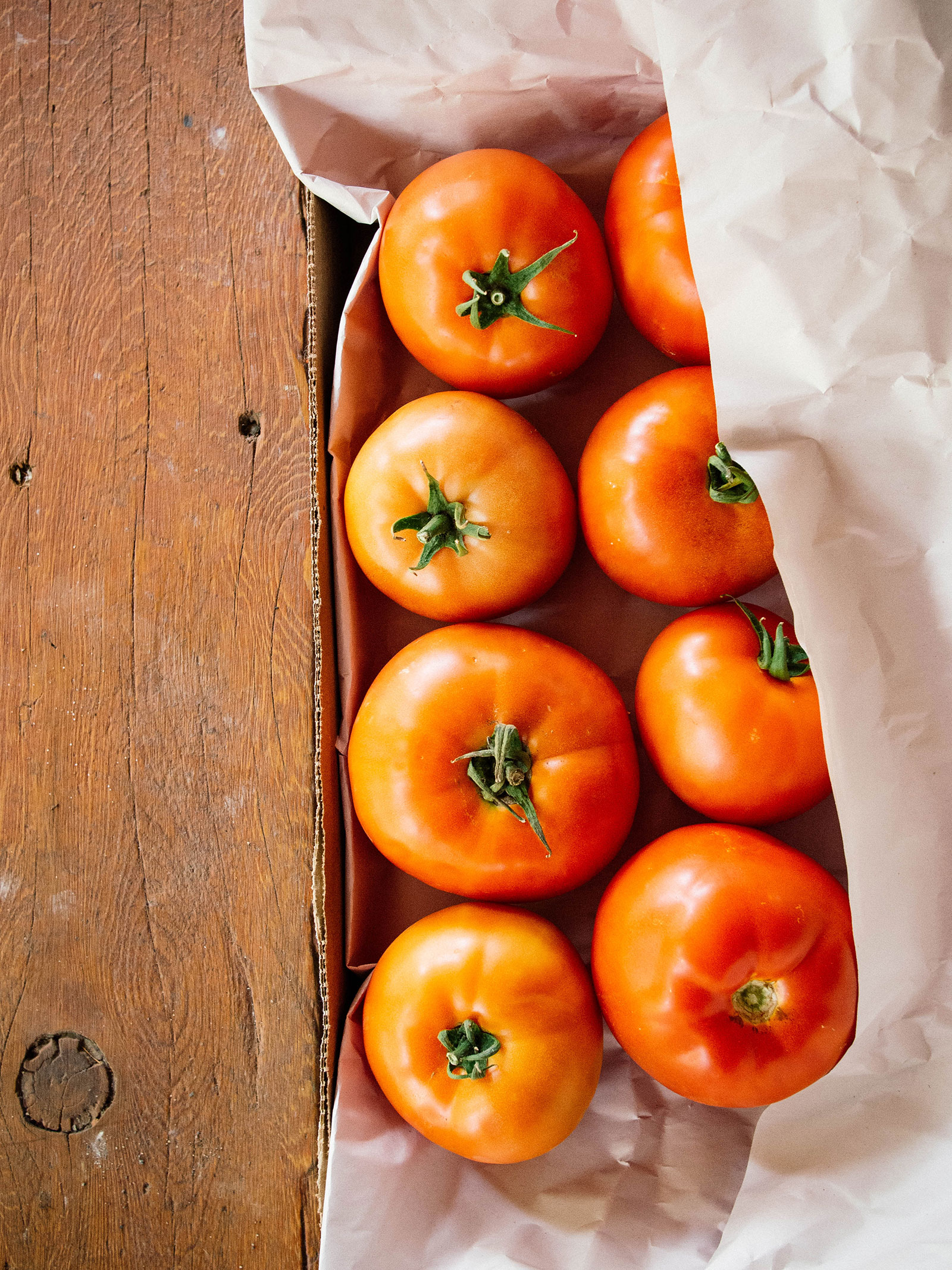 Overhead view of beefsteak tomatoes ripening in a cardboard tray with sheets of newsprint